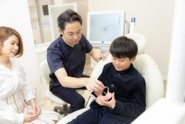 歯の模型を触る子供とそれを見守る歯科医師、母親